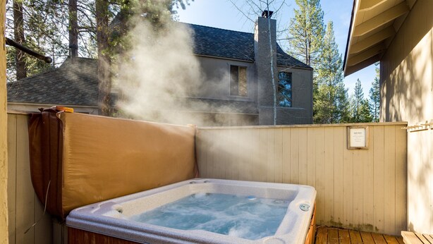 A hot tub in a wooden deck area with a house in the background. - Augusta 4 (Bend)
