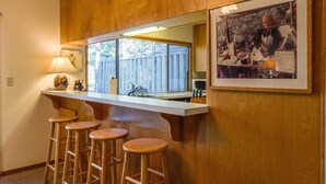 A bar area with wooden stools, a counter, and a large mirror. - Augusta 4 (Bend)