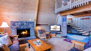A cozy living room with a stone fireplace, a television, and a staircase leading to an upper level.
