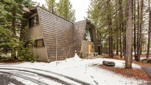 A modern house with a sloped roof, surrounded by tall trees and a snow-covered driveway.
