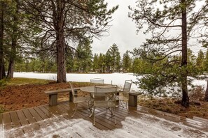 A wooden deck with a metal table and chairs overlooking a snowy landscape with trees. - Augusta 5 (Bend)