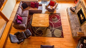 A spacious living room with a wooden floor, a large sectional sofa, a small table, and a stone fireplace. - Bachelor 5 (Bend)