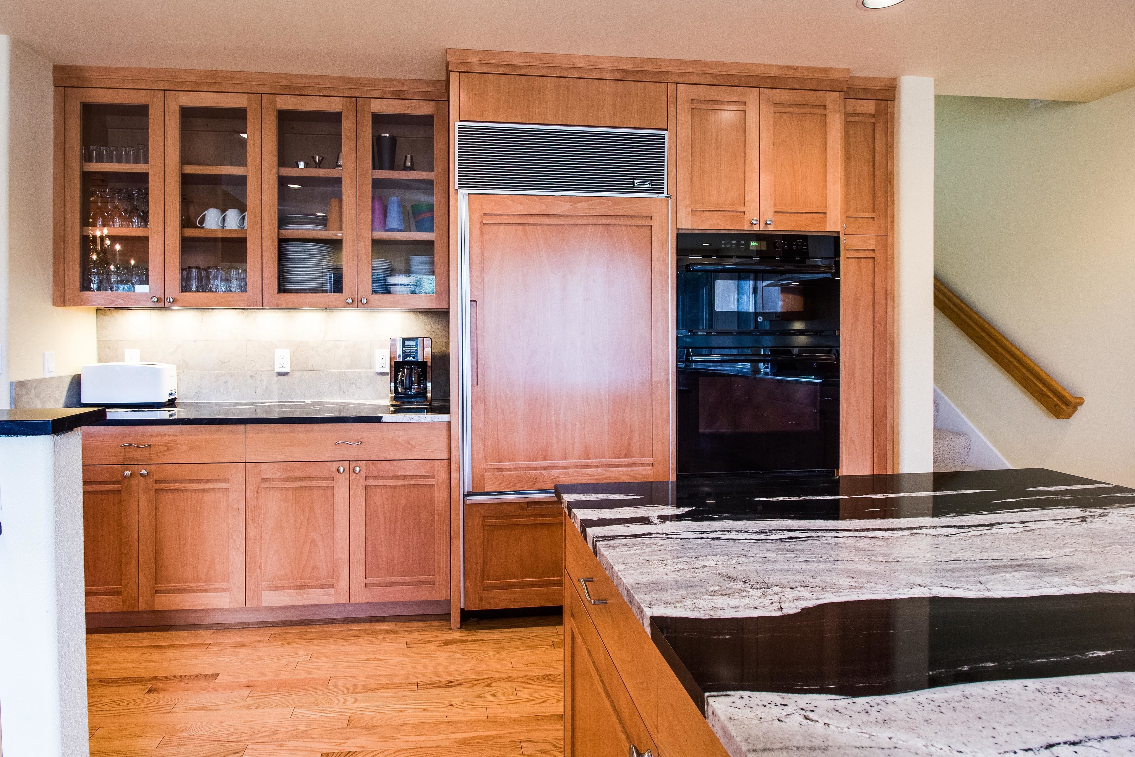 A kitchen with wooden cabinets, a refrigerator, an oven, and a marble countertop.