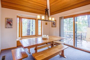 Enjoy meals and gatherings in this dining area with a large table, high ceiling, and beautiful views of the surrounding forest.
