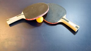 Dos palas de tenis de mesa y una pelota amarilla sobre una superficie oscura.