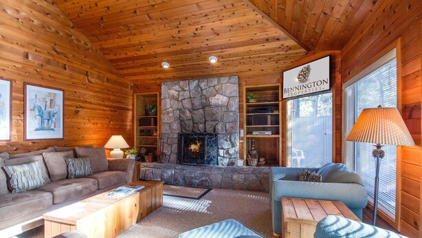 Interior acogedor de una cabaña de troncos con chimenea de piedra, mobiliario de madera y un letrero de Bennington Properties.