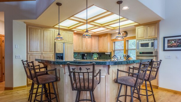 A kitchen with wooden cabinets, a central island with bar stools, pendant lighting, and a microwave.