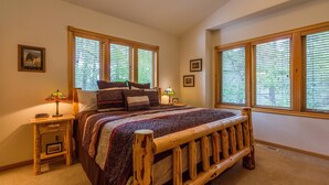 A bedroom with a wooden bed frame, two bedside tables, a lamp, and a window with blinds.