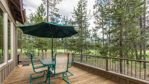 A wooden deck with a table and chairs, an umbrella, and a view of a forested area.