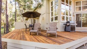 A wooden deck with Adirondack chairs and a grill, surrounded by tall trees. - Big Leaf 25 (Bend)