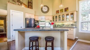 A kitchen with a central island, two bar stools, a refrigerator, and a clock on the wall. - Big Leaf 25 (Bend)