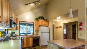 A kitchen with wooden cabinets, a refrigerator, a dishwasher, and a window with a view of trees. - Lark 7 (Bend)