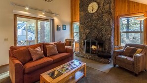 A cozy living room with a stone fireplace, a large window, and a red sofa. - Lark 7 (Bend)