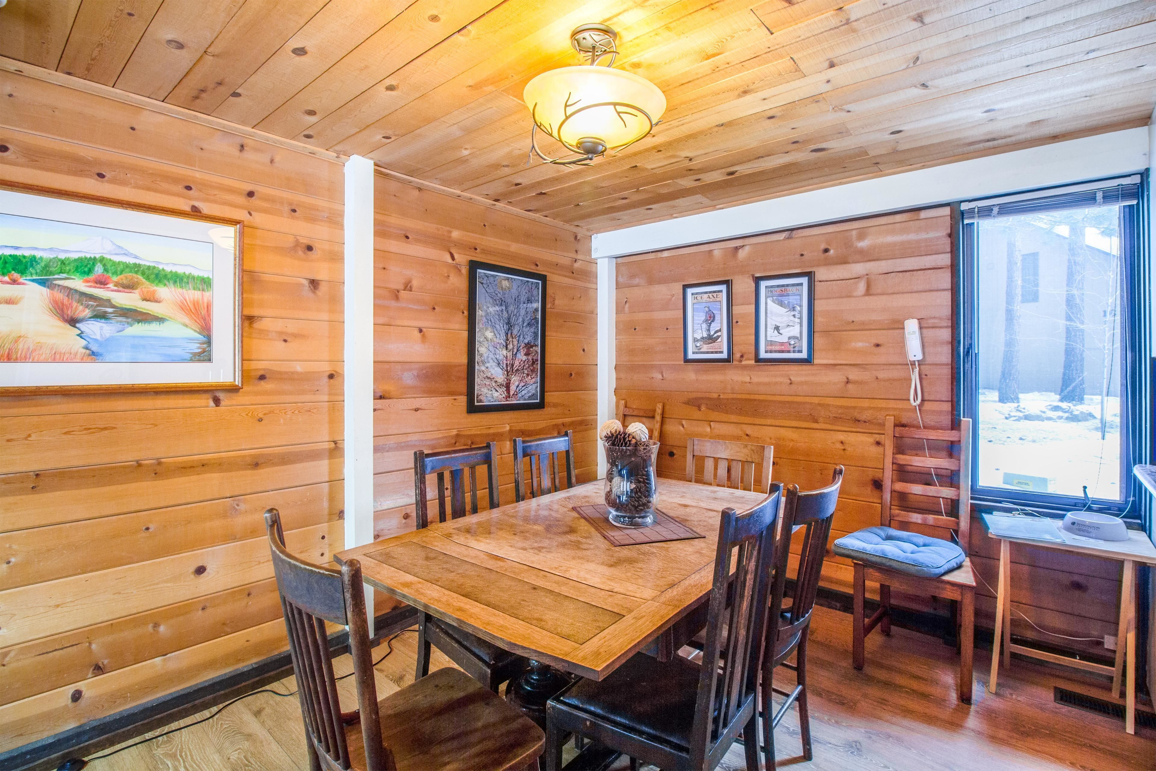 A wooden-paneled dining area with a table, chairs, and framed artwork on the walls.