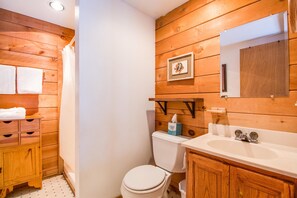 A wooden-paneled bathroom with a white toilet, a sink, and a mirror. - Cluster Cabin 12 (Bend)
