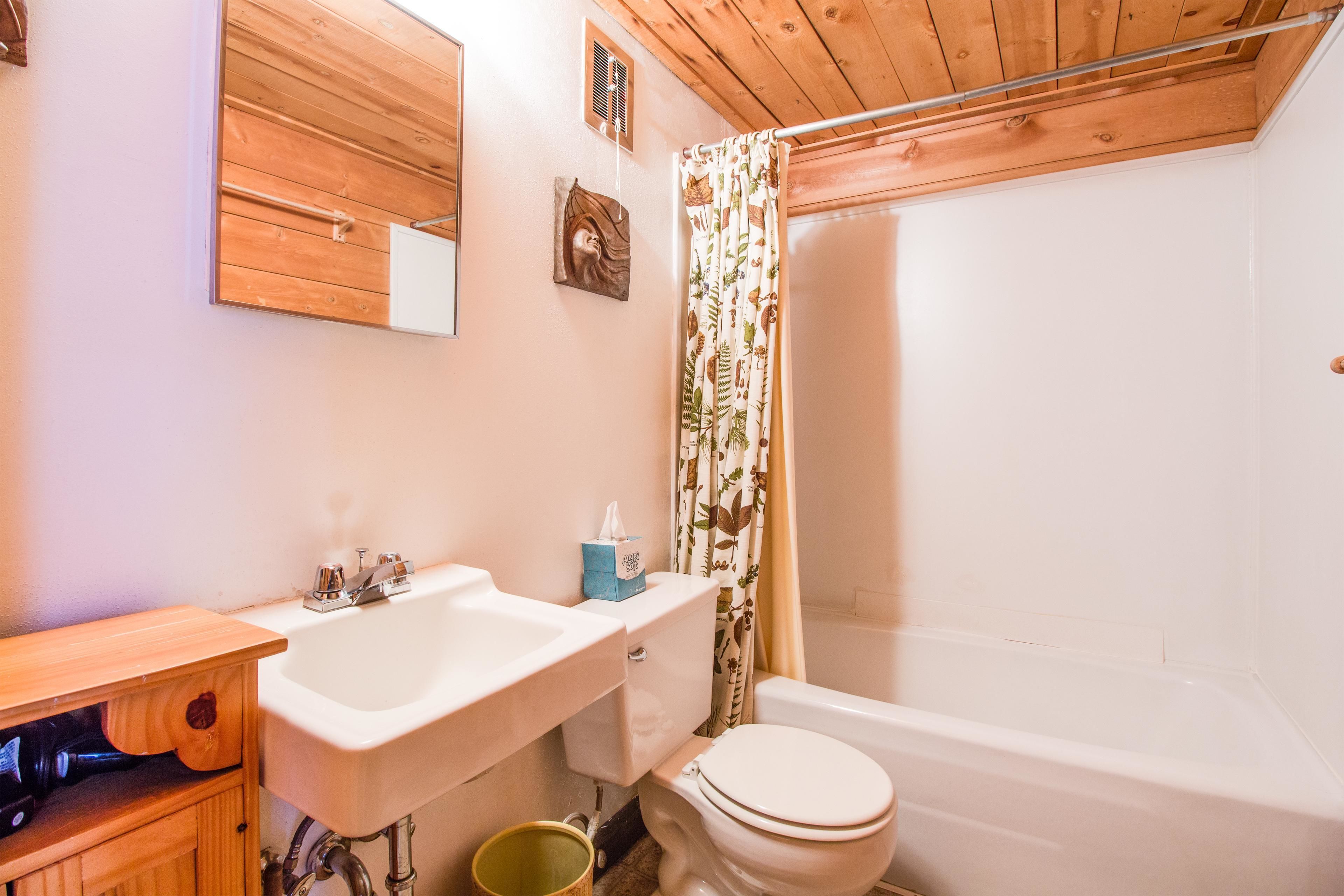 A bathroom with a wooden ceiling, a white sink, a toilet, and a bathtub.