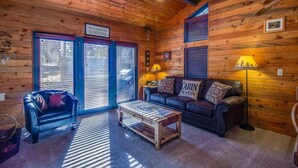 A cozy cabin interior with wooden walls, a leather sofa, a coffee table, and a sign reading "Cabin Fever". - Coyote 8 (Bend)