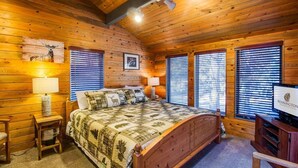 A cozy log cabin bedroom with a large bed, wooden walls, and a television. - Coyote 8 (Bend)