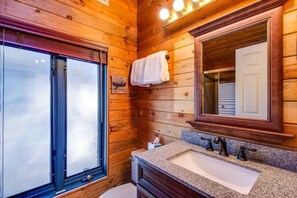 Un baño de cabaña de madera con un ventanal grande, un lavabo con dos grifos y una toalla colgada en la pared.