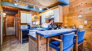A compact kitchen with wooden walls, a central island with bar stools, a microwave, stove, and a sink. - Coyote 8 (Bend)