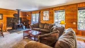 A cozy cabin interior with a stone fireplace, wooden walls, a sofa, and a view of the outdoors. - Coyote 19 (Bend)