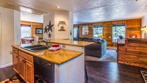 A spacious living area with a kitchen island, wooden walls, and large windows. - Coyote 19 (Bend)