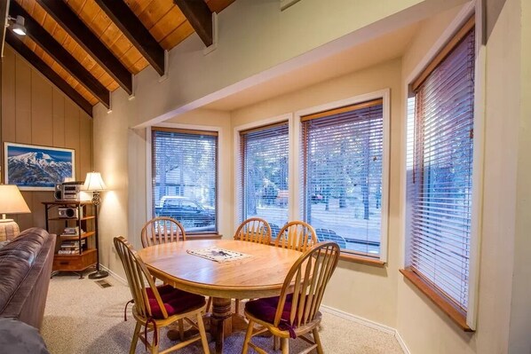 Cozy dining area with a round table and six chairs, offering a view of the outside through large windows.