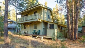 A two-story cabin with a balcony, surrounded by trees. - Deer 10 (Bend)
