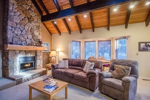 Un salon chaleureux avec une cheminée en pierre, des poutres apparentes en bois et un coin salon confortable.