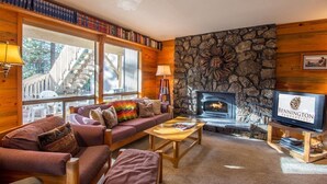 Una sala de estar acogedora con chimenea de piedra, televisor y una estantería llena de libros.