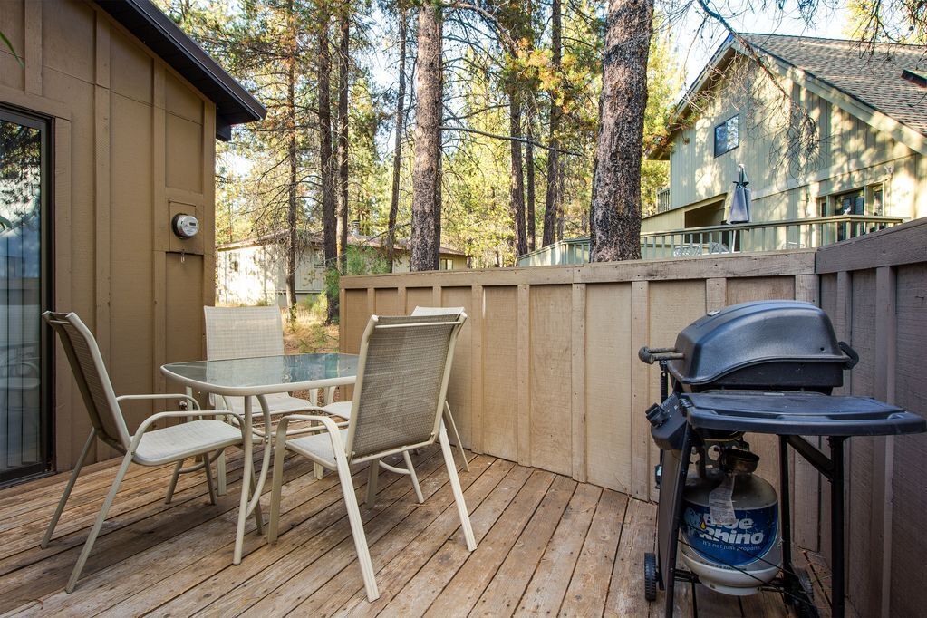 A deck with a glass table and chairs, a barbecue grill, and a propane tank.