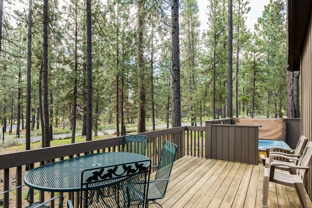A wooden deck with a table and chairs, surrounded by tall pine trees.