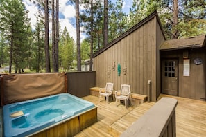 A wooden deck with a hot tub, two chairs, and a bench.