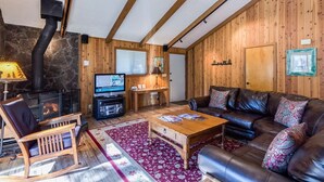 A cozy living room with a stone fireplace, wooden walls, a leather sofa, and a television. - Diamond Peak 23 (Bend)