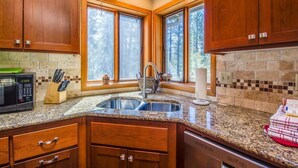 A kitchen with wooden cabinets, a granite countertop, a double sink, and a microwave. - Diamond Peak 4 (Bend)