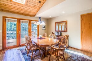 Enjoy meals in this dining area with a wooden table and six chairs, surrounded by a large window with a view of the woods.