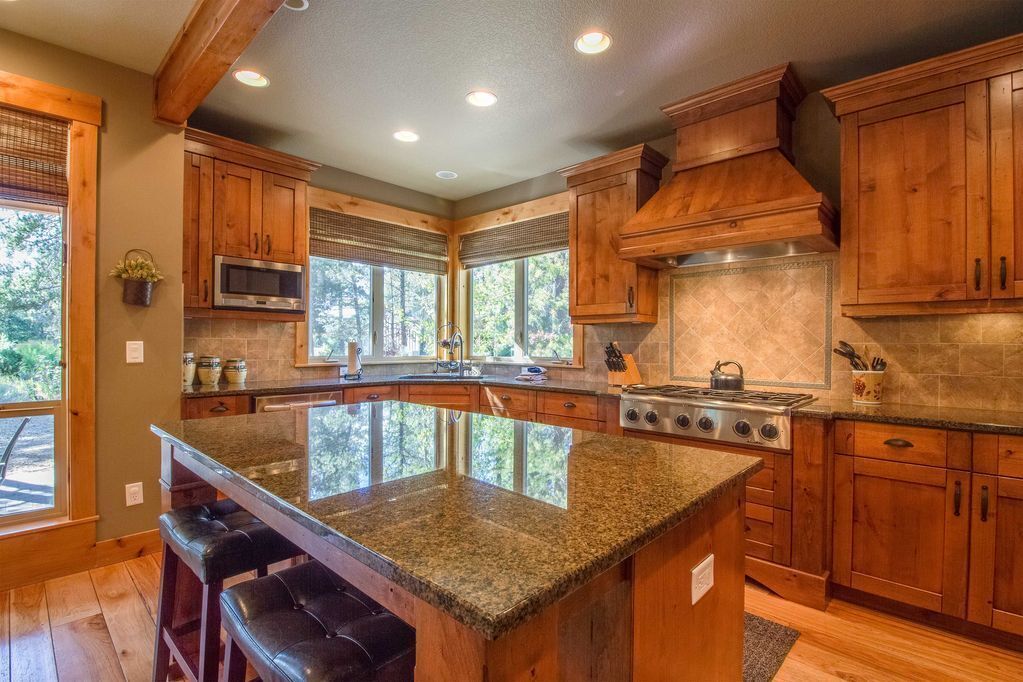 Une cuisine spacieuse avec des meubles en bois, un îlot central doté d’un plan de travail en granit et une grande cuisinière.
