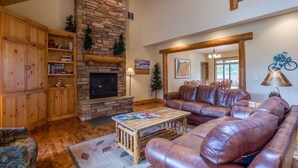 A cozy living room with a stone fireplace, leather sofa, wooden shelves, and a ceiling fan. - Duck Pond 3 (Bend)
