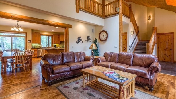 A spacious living room with a large brown leather sectional sofa, a wooden coffee table, and a dining area with wooden chairs and a wooden table. - Duck Pond 3 (Bend)