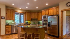 A spacious kitchen with wooden cabinets, stainless steel appliances, and a large island with bar stools. - Duck Pond 3 (Bend)