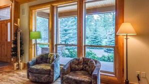 A room with two armchairs, a lamp, and large windows with a view of trees. - Duck Pond 3 (Bend)