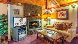 A cozy living room with a stone fireplace, a television, and a sofa. - East Butte 10 (Bend)