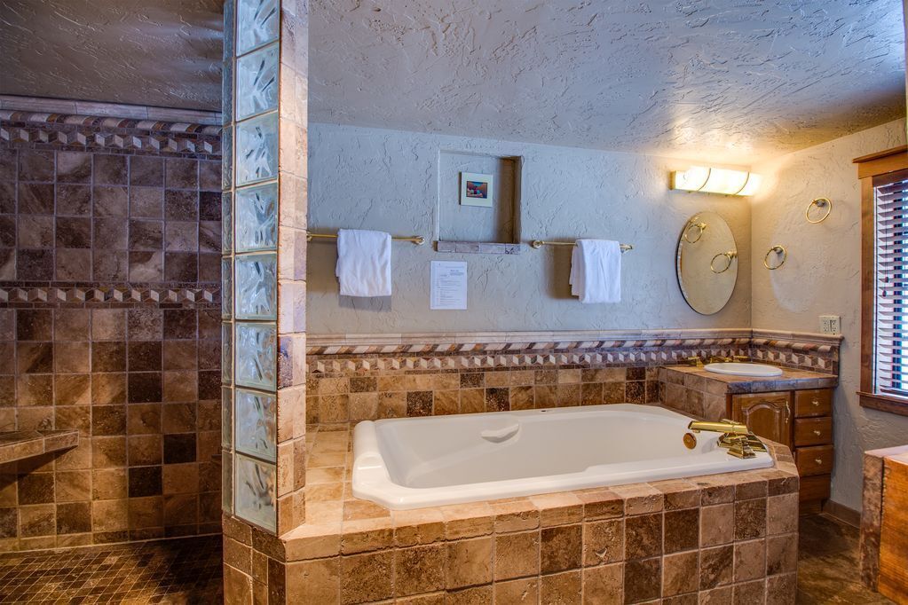 Ein Badezimmer mit einer großen Badewanne, einem Waschbecken und einem Spiegel. Handtücher hängen an einem Wäscheständer und es gibt ein kleines Regal mit einem Bild.