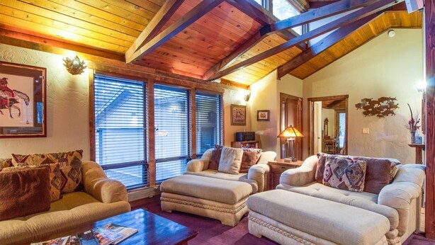 A cozy living room with a high wooden ceiling, a fireplace, and a large window with blinds. - East Butte 10 (Bend)