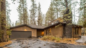 A modern log cabin with a stone chimney, a garage, and a wooden deck. - East Butte 10 (Bend)