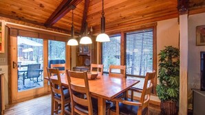 A wooden dining table with six chairs, a hanging light fixture, and a potted plant. - East Butte 10 (Bend)