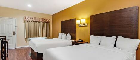 A hotel room with two beds, a wooden floor, a door, and a curtain.
