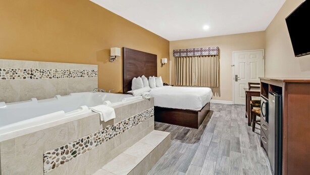 Une chambre d’hôtel avec une grande baignoire, un lit, un bureau avec une chaise et un téléviseur fixé au mur.
