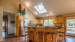 A modern kitchen with a skylight, wooden cabinets, a central island with bar stools, and a refrigerator. - Red Cedar 49 (Bend)