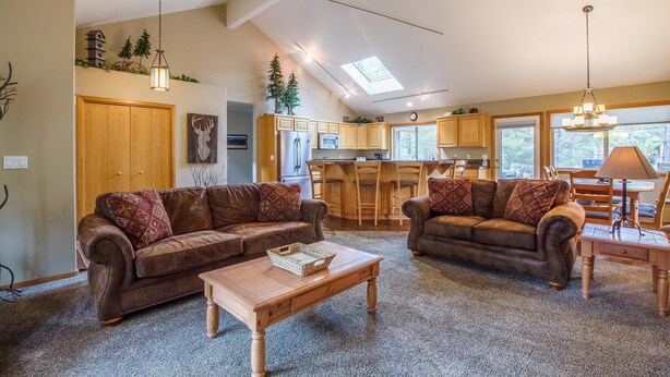 A spacious living room with two brown leather sofas, a wooden coffee table, and a kitchen in the background. - Red Cedar 49 (Bend)